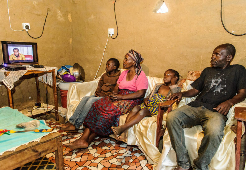 Cecelia Miti watches television with her son Godfrey and her grandchildren